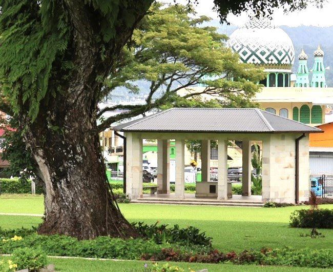 A shelter in the landscaped cemetery grounds, with a mosque's domes beyond the trees