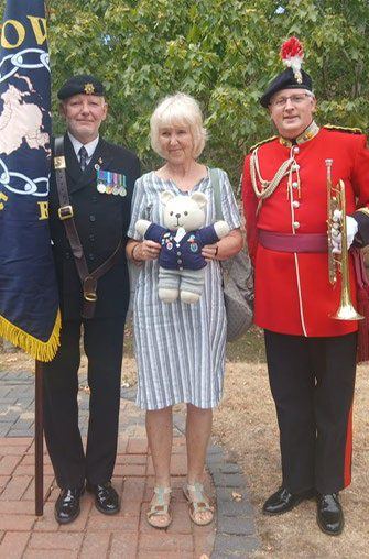 A standard bearer, a member holding a teddy bear and a bugler in ceremonial red uniform