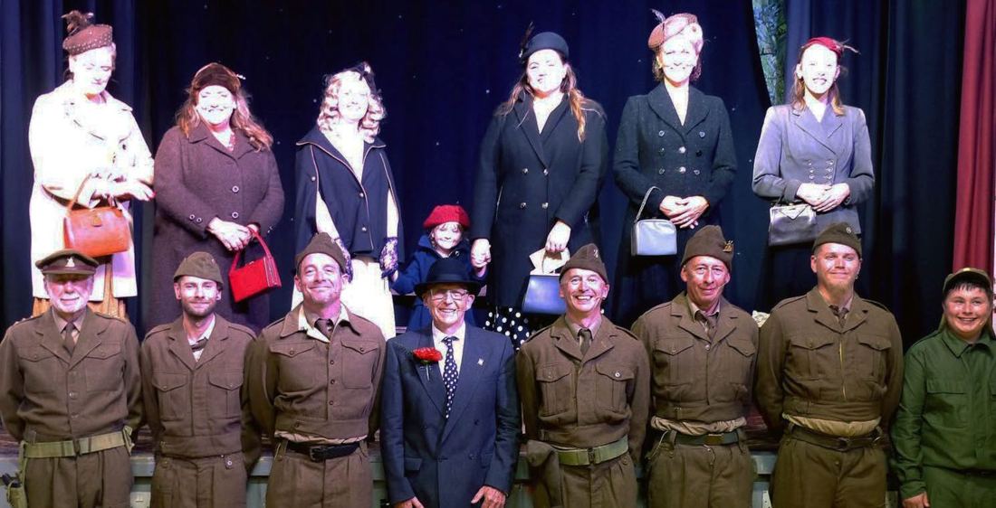 The full cast in 1940s costume and uniform lined up on stage